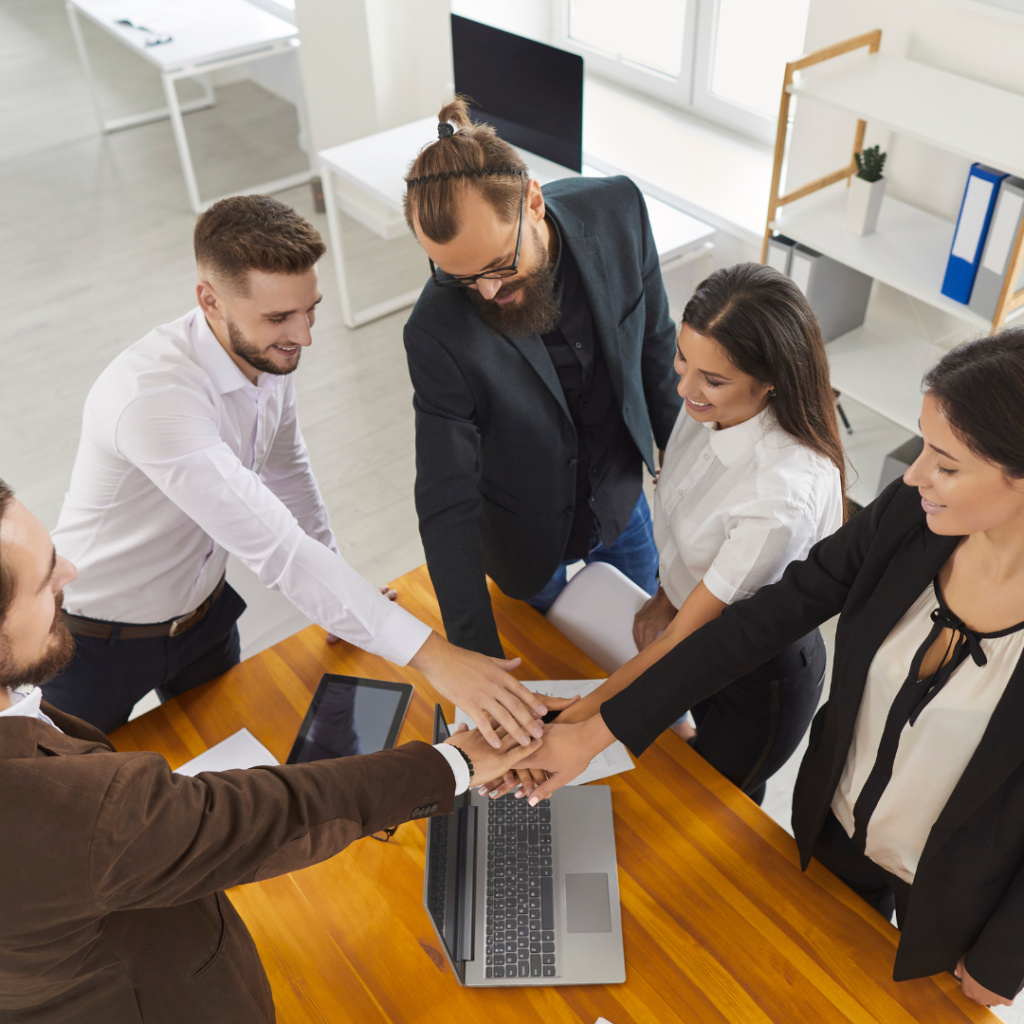 Equipo de profesionales uniendo sus manos en símbolo de colaboración, representando el trabajo en conjunto en una Unión Temporal de Empresas (UTE), con documentos y tecnología sobre la mesa en un entorno de oficina.