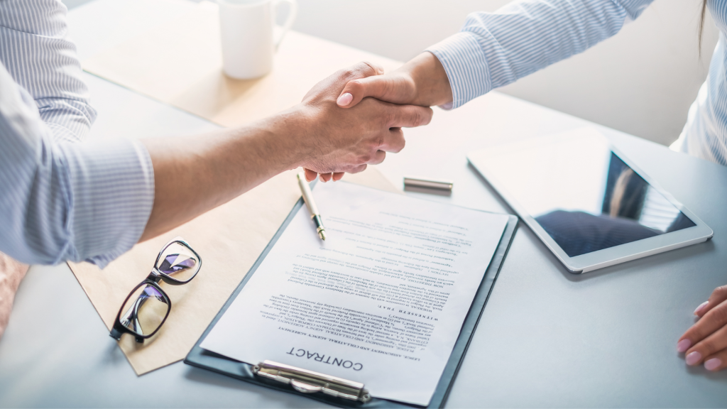 Dos personas estrechándose la mano frente a un contrato sobre una mesa, representando acuerdos legales en contratos de distribución internacional en España. Imagen destacada del artículo 'Aspectos legales de los contratos de distribución internacional en España'