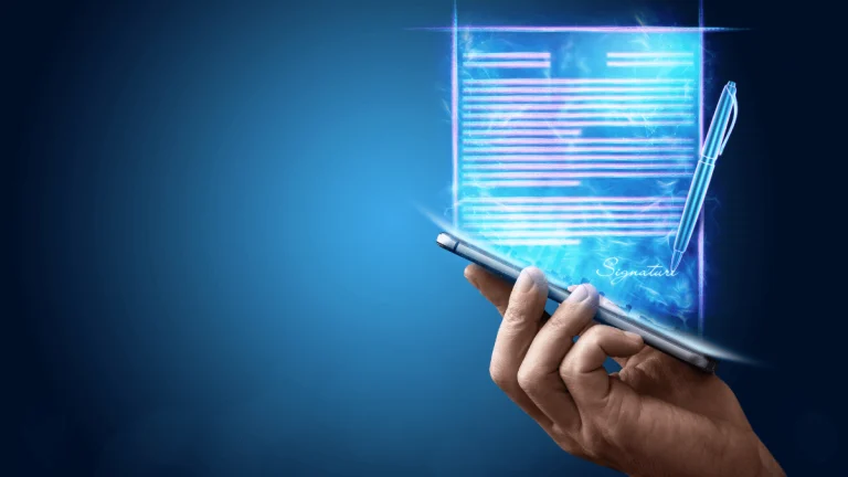 Una mano sostiene un teléfono móvil del que emerge un documento digital en forma de holograma azul brillante. El documento muestra líneas de texto y una firma digital al pie, junto a una pluma estilográfica también holográfica. El fondo es un degradado azul oscuro que resalta el efecto futurista de la escena. La imagen transmite el concepto de firma electrónica y digitalización de documentos en un entorno tecnológico avanzado.