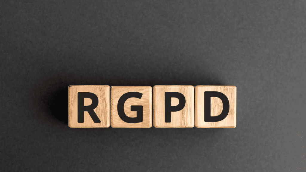 Cuatro bloques de madera alineados horizontalmente sobre un fondo gris oscuro, cada uno con una letra negra en mayúscula que en conjunto forman el acrónimo “RGPD”, siglas del Reglamento General de Protección de Datos, normativa europea sobre privacidad y protección de datos personales.