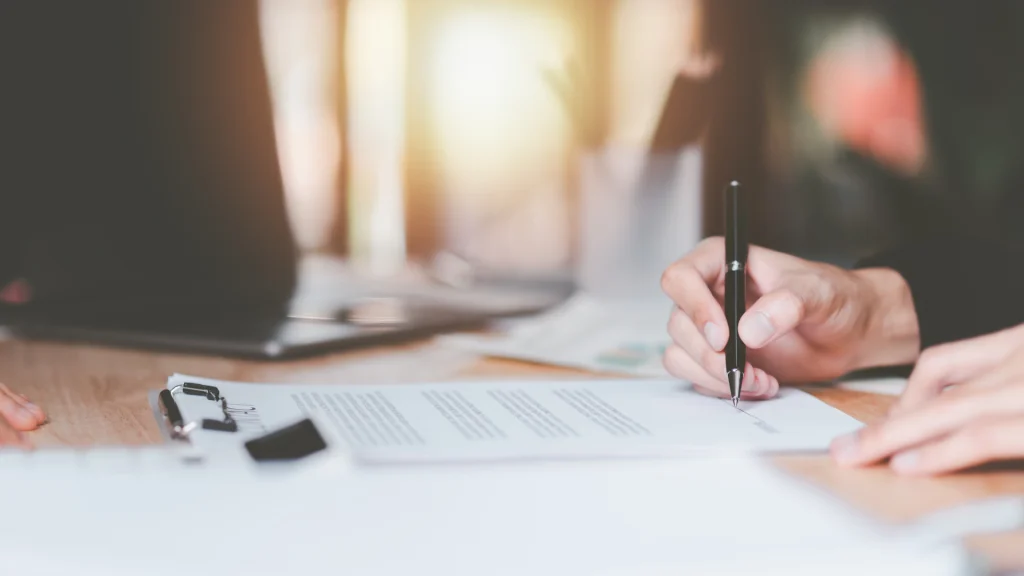 Persona firmando un contrato de prestación de servicios sobre una mesa de oficina