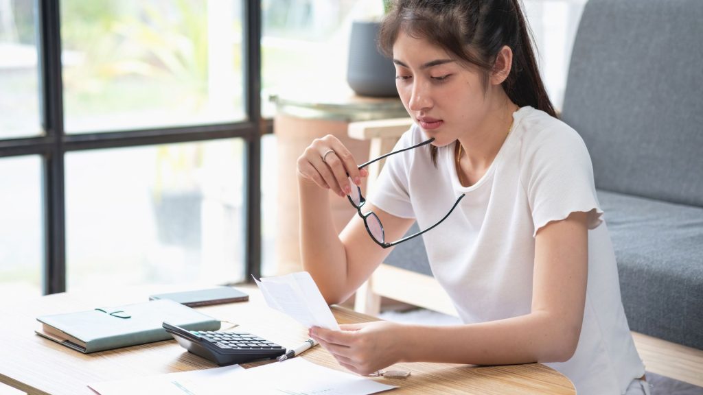 Mujer con semblante serio revisando un documento sobre el reintegro de prestaciones indebidas, con una calculadora y documentos en la mesa.