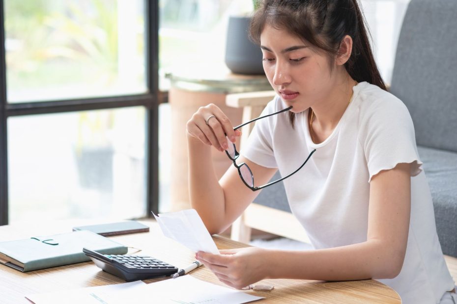 Mujer con semblante serio revisando un documento sobre el reintegro de prestaciones indebidas, con una calculadora y documentos en la mesa.