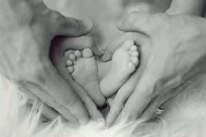 Manos de dos adultos formando un corazón alrededor de los pies de un bebé, representando el vínculo familiar en un divorcio