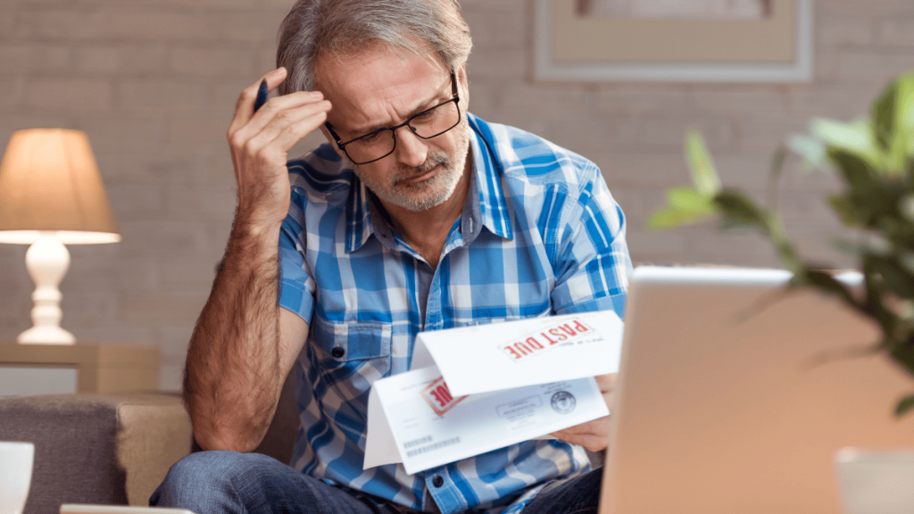Hombre de mediana edad con gafas y expresión preocupada, sentado en una sala de estar doméstica, revisa una carta con el aviso “PAGO VENCIDO” (Past Due) en letras rojas. Sostiene su frente con una mano en señal de estrés mientras observa el documento. Frente a él hay una computadora portátil encendida, lo que sugiere que está revisando información financiera o comunicándose en línea. La escena transmite las consecuencias personales de un concurso de acreedores internacional, reflejando el impacto económico en los individuos afectados.