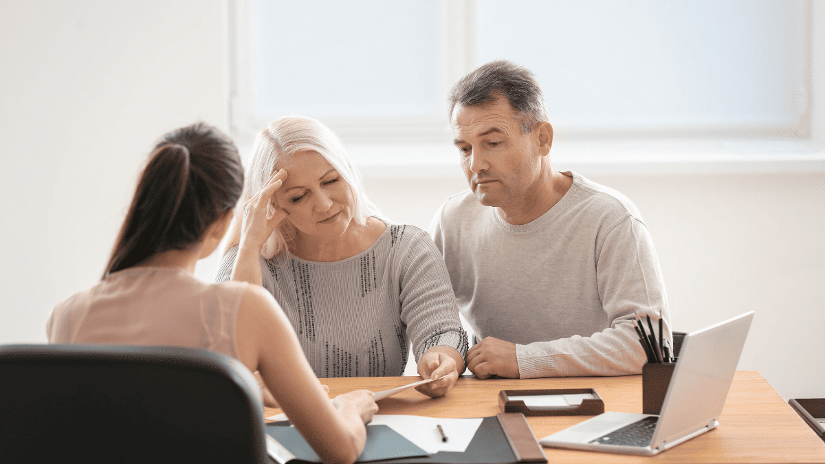 Pareja madura preocupada revisando documentos con una asesora legal en una oficina, representando las dificultades de las herencias internacionales y el uso del Certificado Sucesorio Europeo.