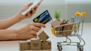 Carrito de compra con cajas de envío y una persona realizando una compra online con tarjeta de crédito, representando la reventa internacional y el comercio electrónico global.
