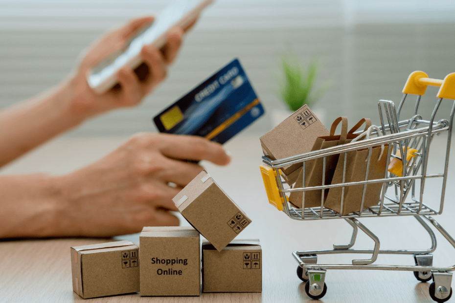 Carrito de compra con cajas de envío y una persona realizando una compra online con tarjeta de crédito, representando la reventa internacional y el comercio electrónico global.