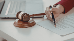 Mano firmando un documento legal junto a un mazo de juez, relacionado con herencias y testamentos en España.