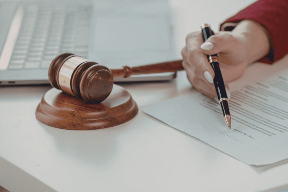 Mano firmando un documento legal junto a un mazo de juez, relacionado con herencias y testamentos en España.