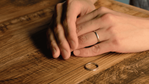 Manos con anillo de boda y otra alianza sobre la mesa, símbolo de separación en un divorcio internacional.