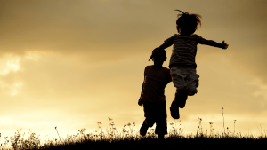 Silhouette of two children jumping in a field at sunset.