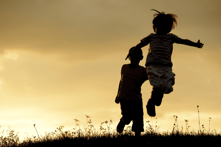 Silueta de dos niños saltando en un campo al atardecer.
