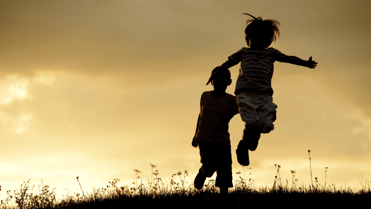 Silueta de dos niños saltando en un campo al atardecer.